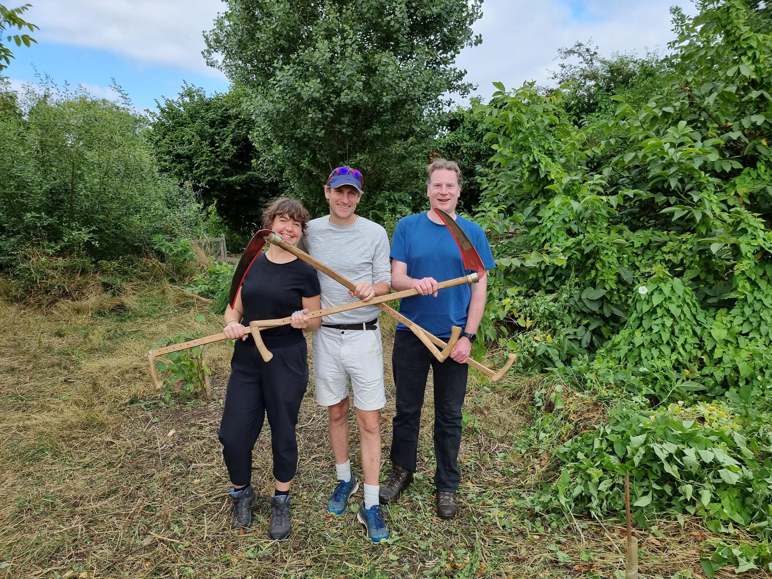 Gemma, Richard and Stephen holding scythes in front of a newly cleared path