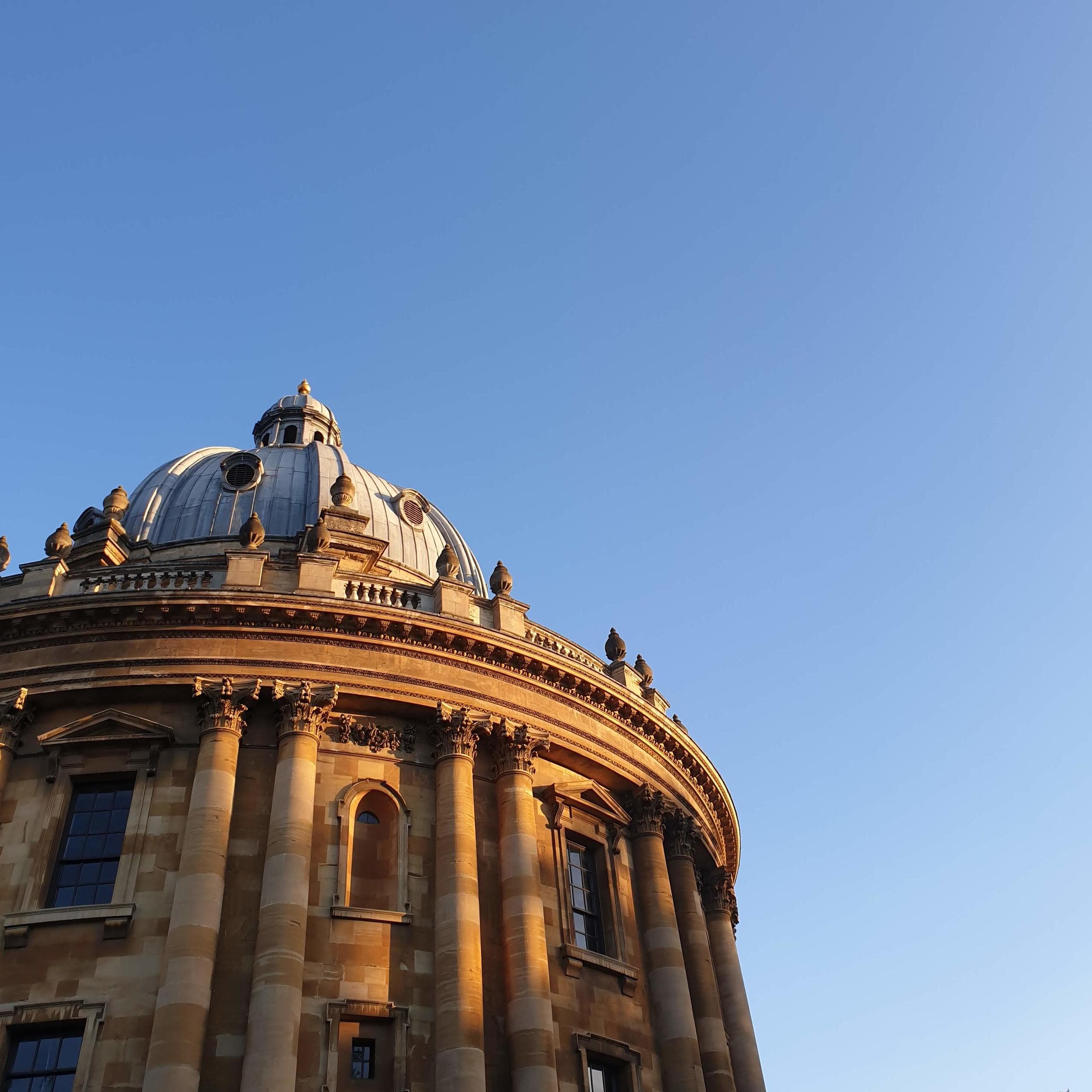 Looking up at the Radcliffe Camera building against blue sky, the builidng has an ornate facade.