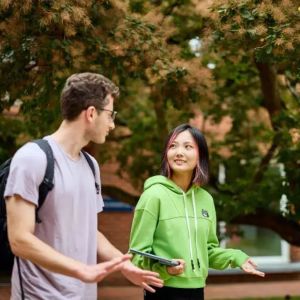 two students walking in front of a tree. One in a t-shirt and one in a hoody