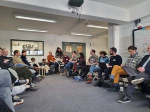 People sitting on chairs in a circle listening to someone talk.