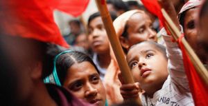 A Bangladeshi boy helps to raise a red flag at a demonstration. He is surrounded by the crowd at the protest, mostly women with headscarves. Credit: Rainbow Collective